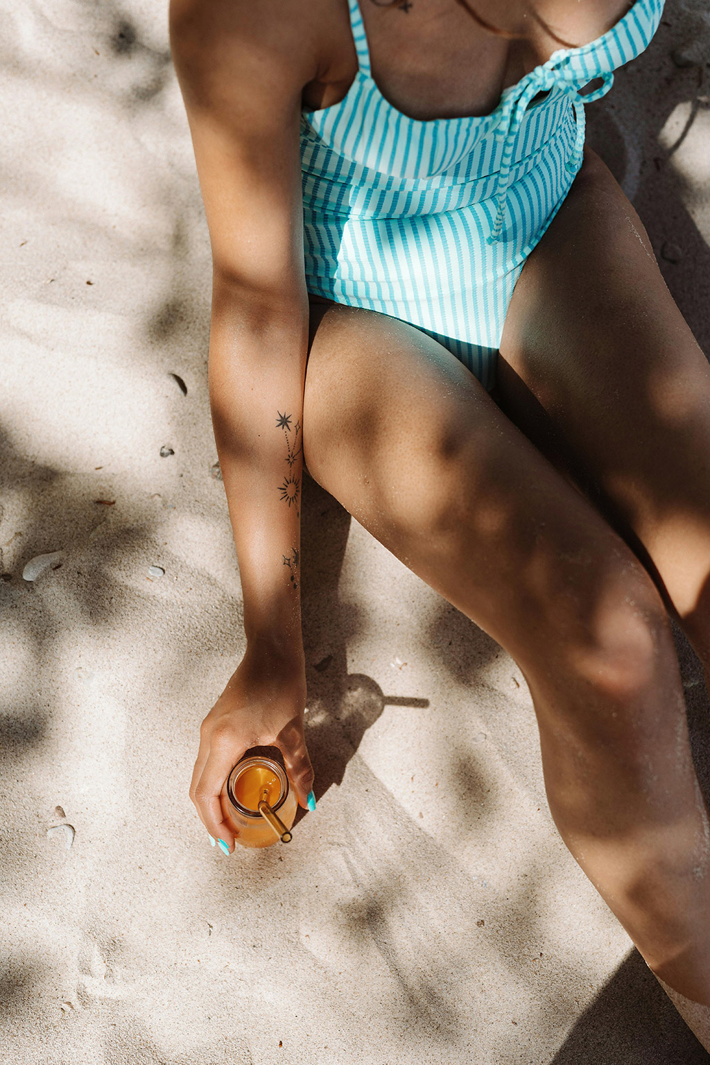 woman on beach with blue bathing suit with alcoholic beverage